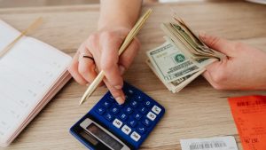 A Person With Cash In Hand Using A Calculator To Make Financial Calculations
